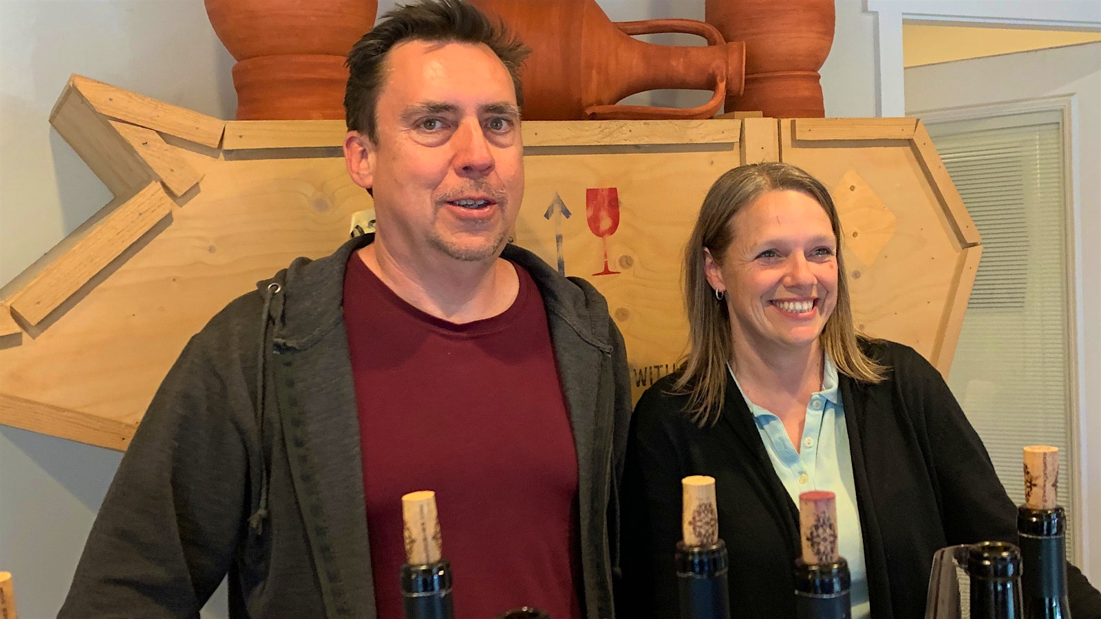 Giornata founders Brian and Stephanie Terrizzi in their tasting room with amphora on the shelf behind them and wine bottles in front